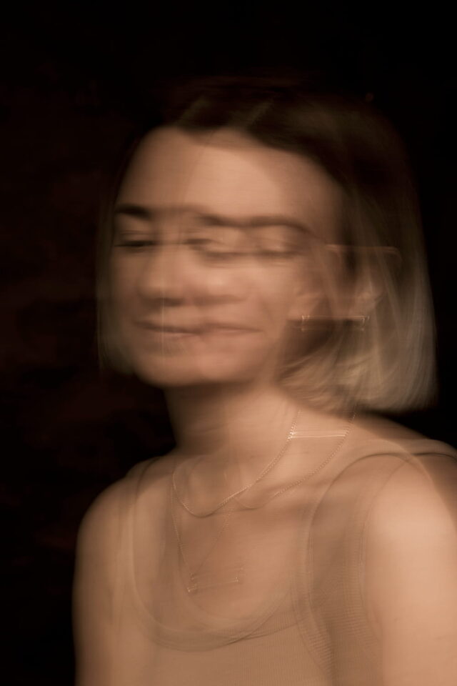 Portrait einer Frau, dargestellt unscharf in Doppelbelichtung. Der Hintergrund ist schwarz.